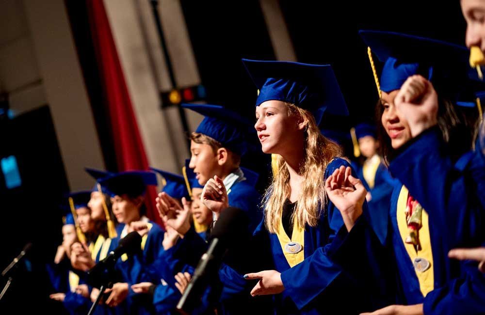 A group of children in graduation caps and gowns are standing on a stage.