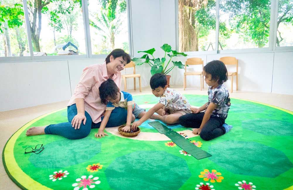 A woman and three children are sitting on a green rug.