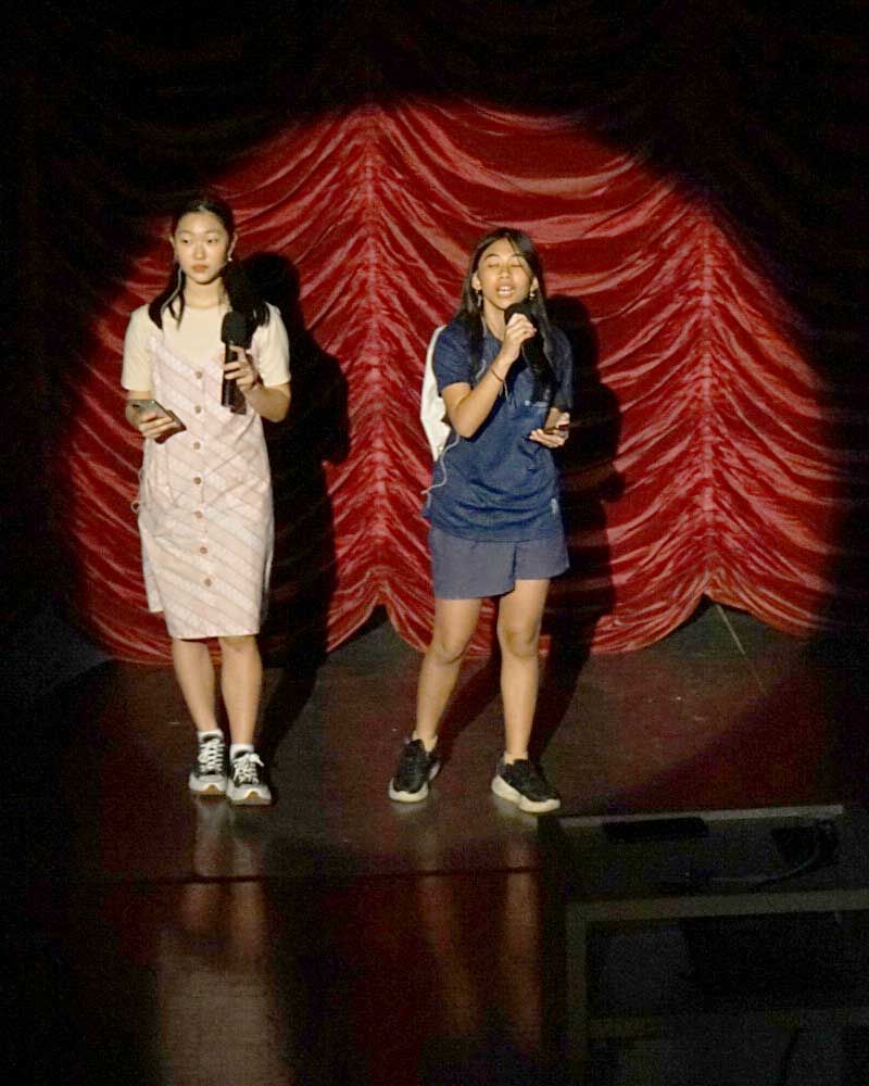 Two girls are standing on a stage holding microphones.