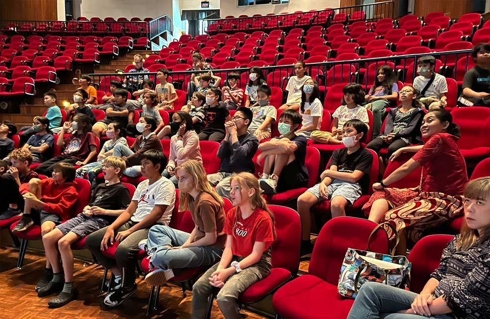 A large group of people are sitting in red chairs in an auditorium.