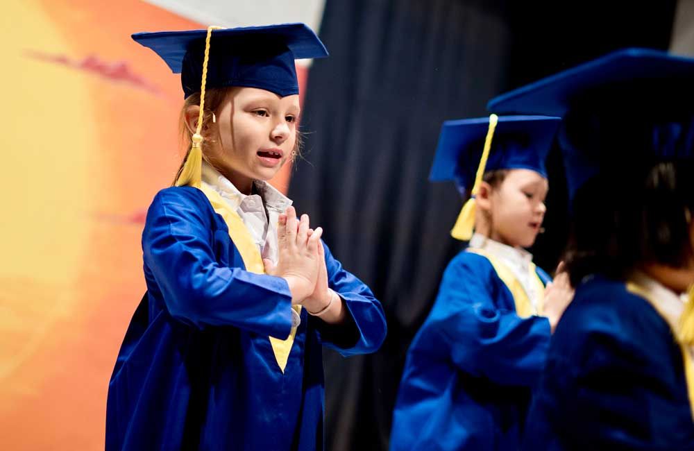 A group of children wearing graduation caps and gowns are standing on a stage.
