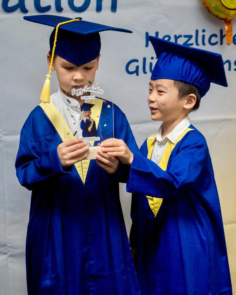 Two young boys in graduation caps and gowns are looking at a picture