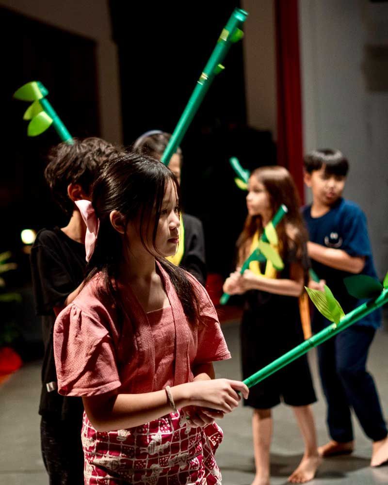 A group of children are holding green sticks with leaves on them