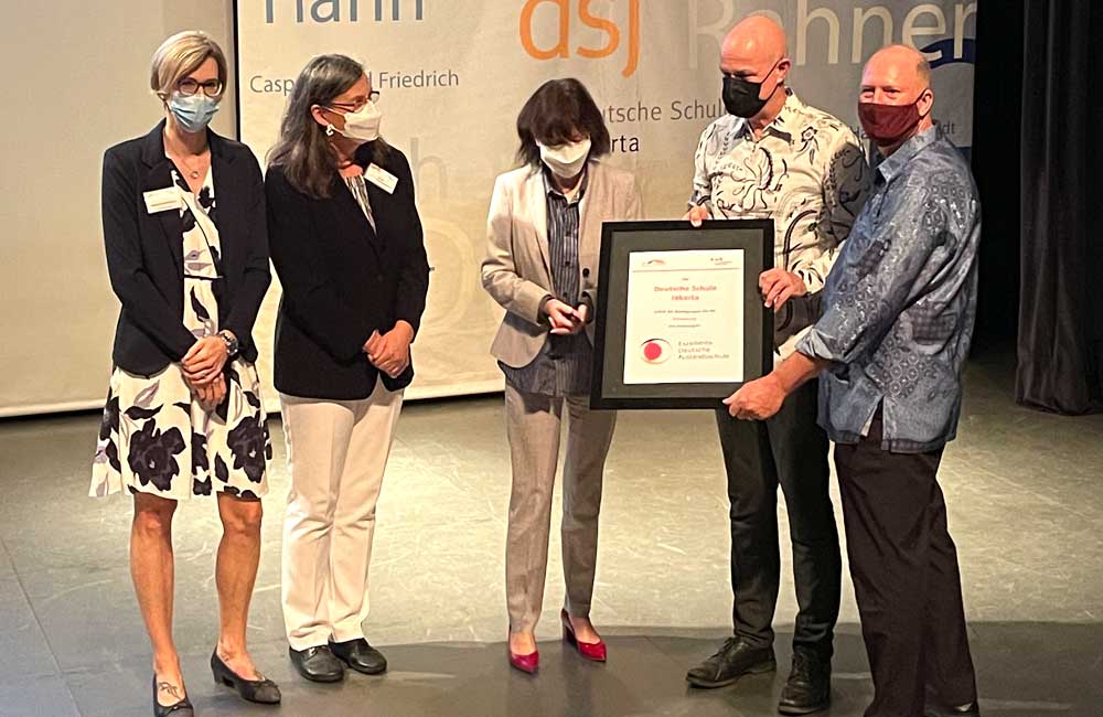 A group of people wearing face masks are standing on a stage holding a framed certificate.