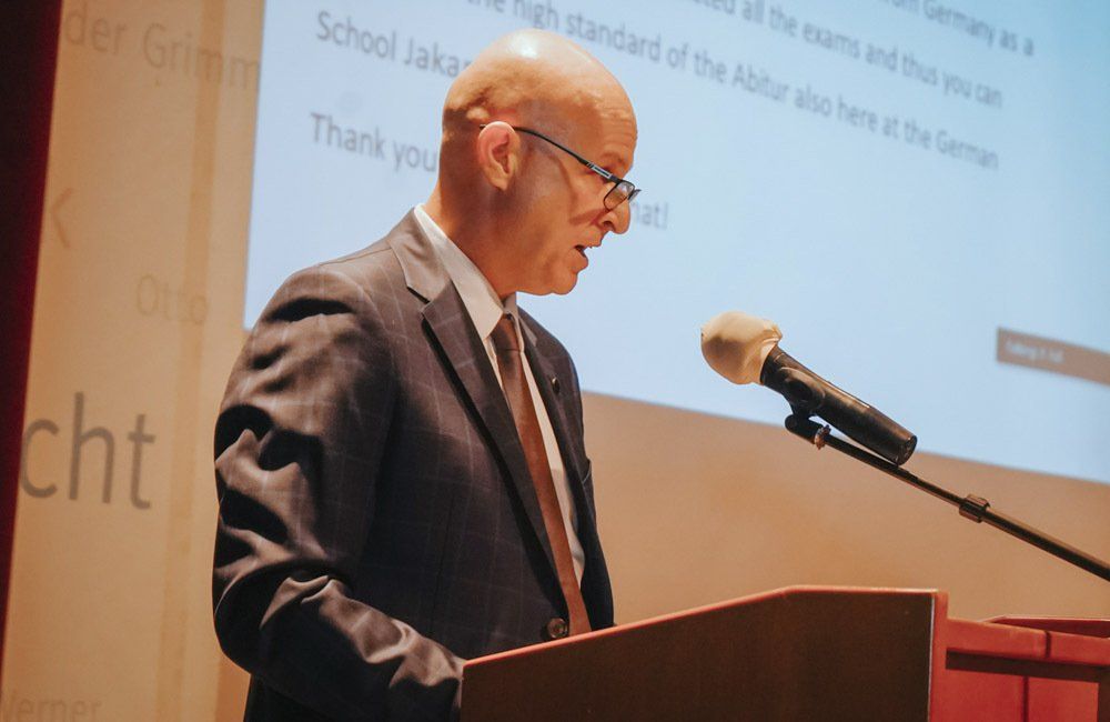 A man in a suit and tie is standing at a podium speaking into a microphone.