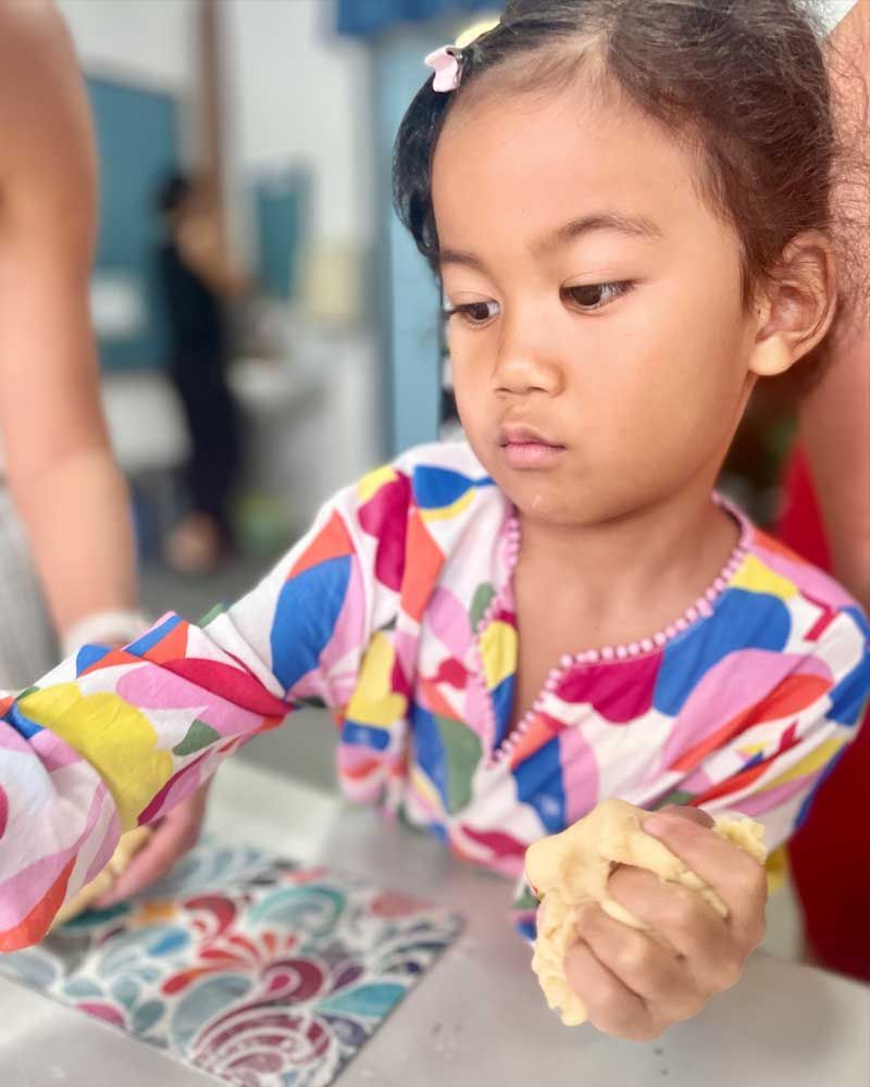 A little girl is sitting at a table playing with dough.
