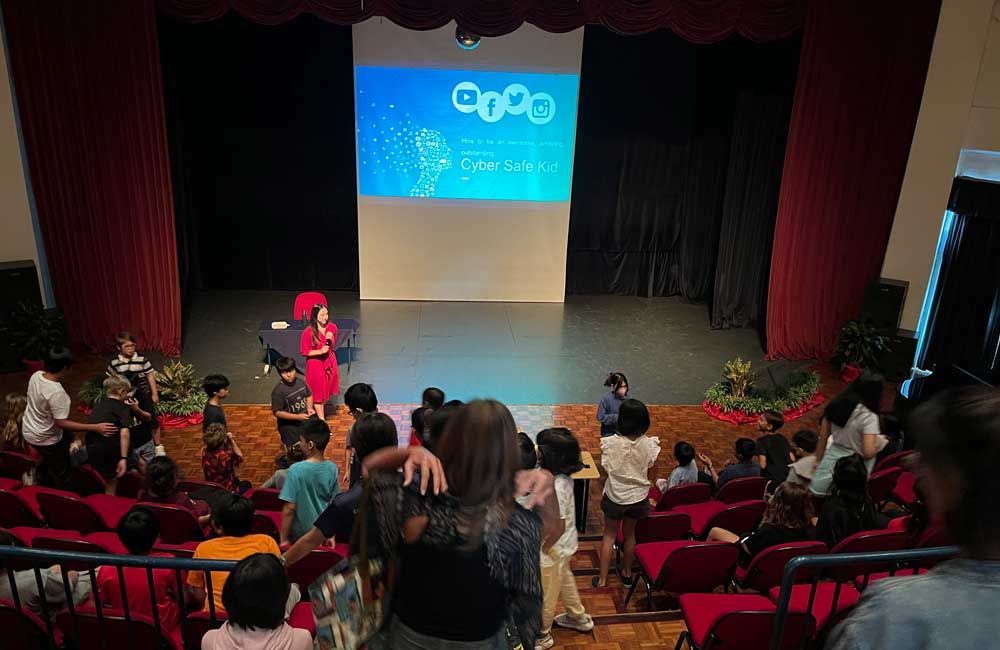 A group of people are sitting in an auditorium watching a presentation on a stage.
