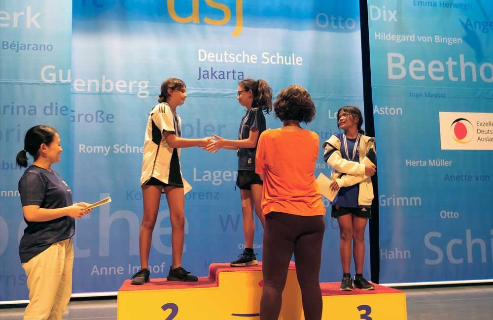 A group of girls shaking hands on a podium in front of a wall that says beethoven