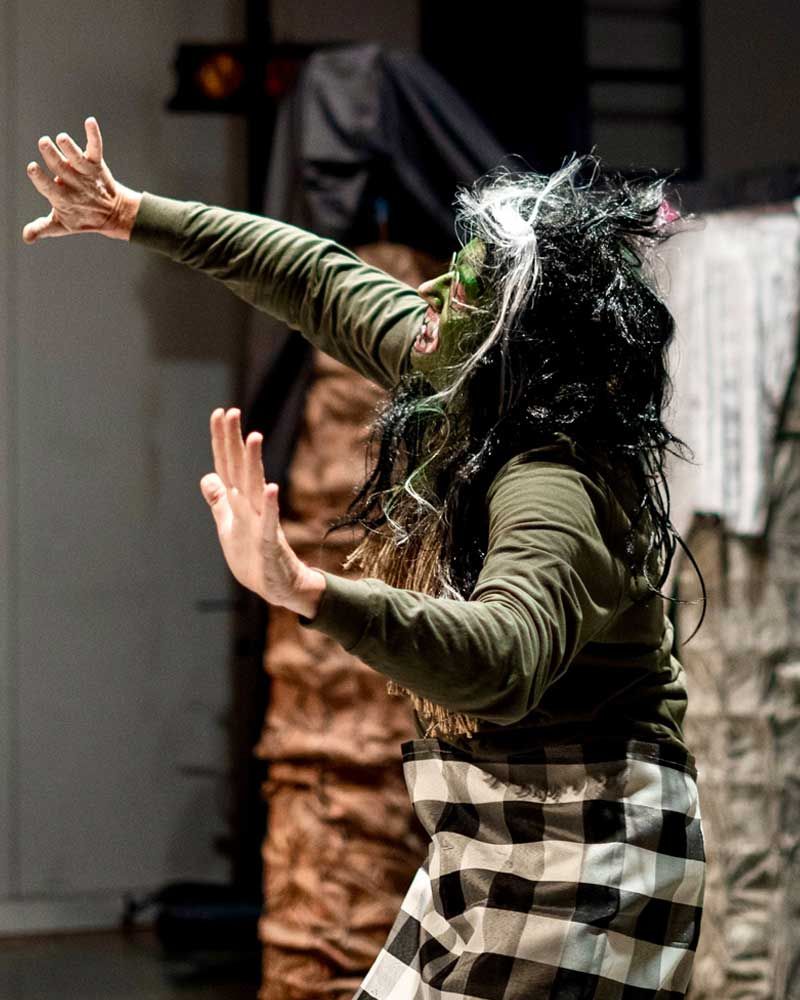 A woman in a green shirt and plaid skirt is dancing on a stage.