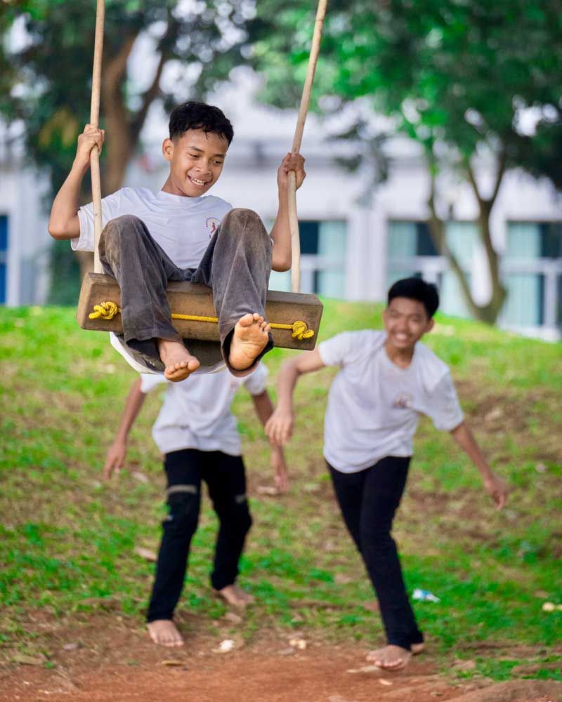 Two young boys are playing on a wooden swing in a park.