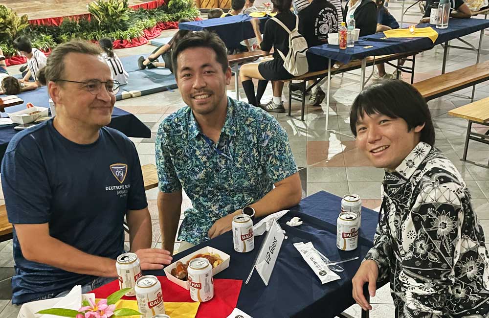 Three men are sitting at a table with cans of beer.