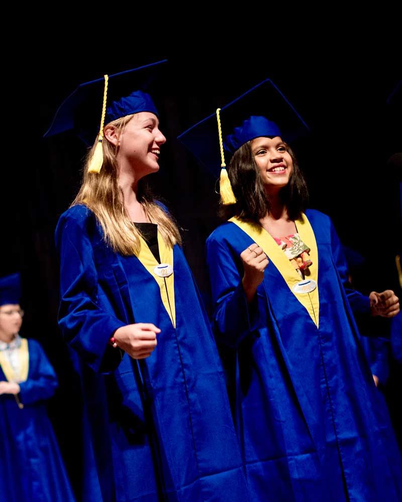 Two female graduates are standing next to each other on a stage.