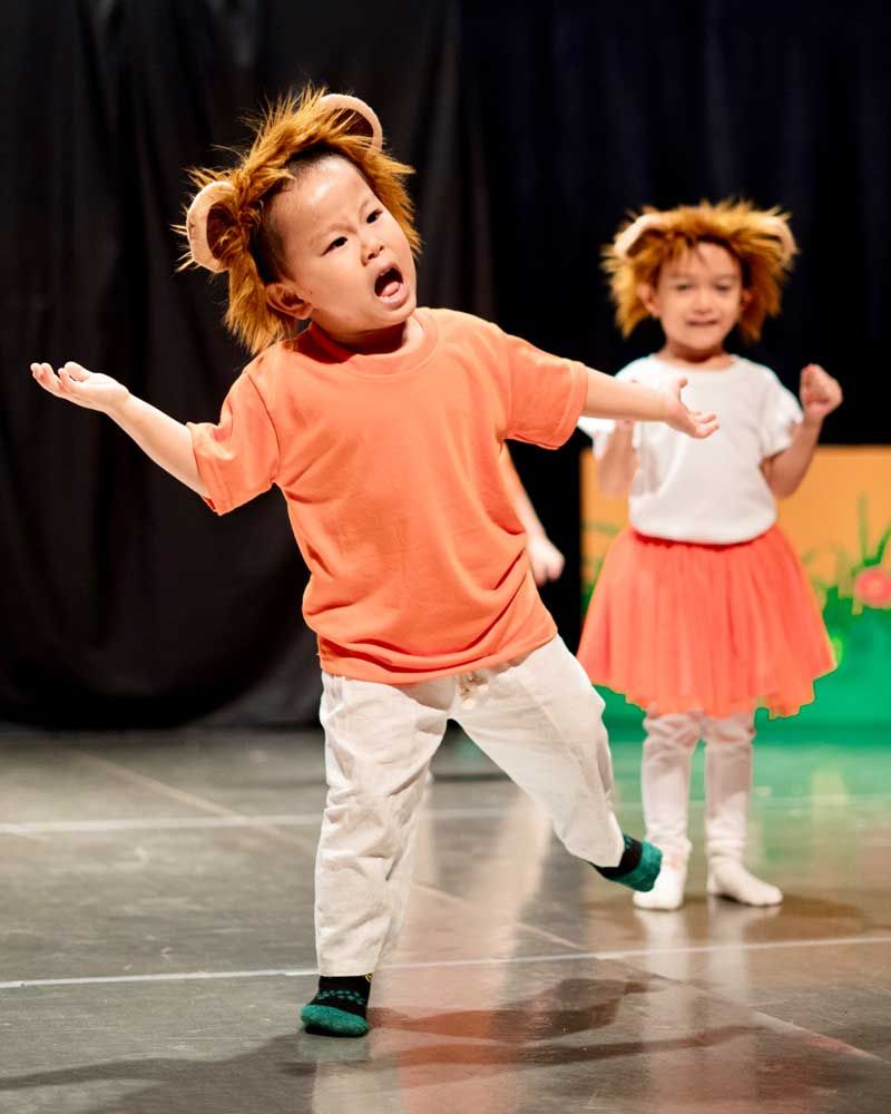 Two little girls are dancing on a stage and one of them is dressed as a lion.