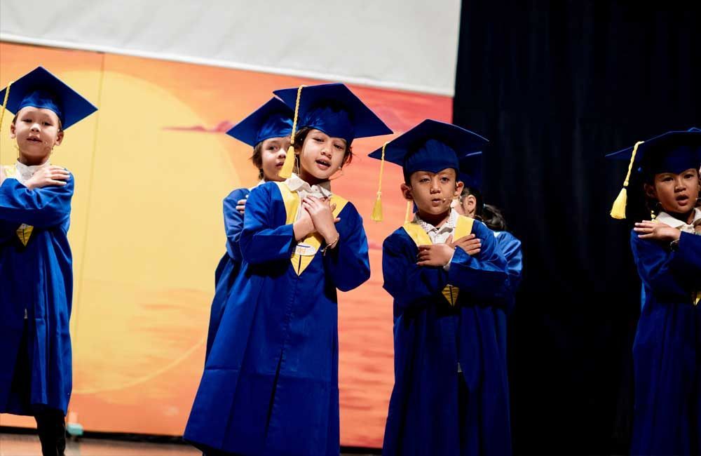A group of children wearing graduation caps and gowns are standing on a stage.