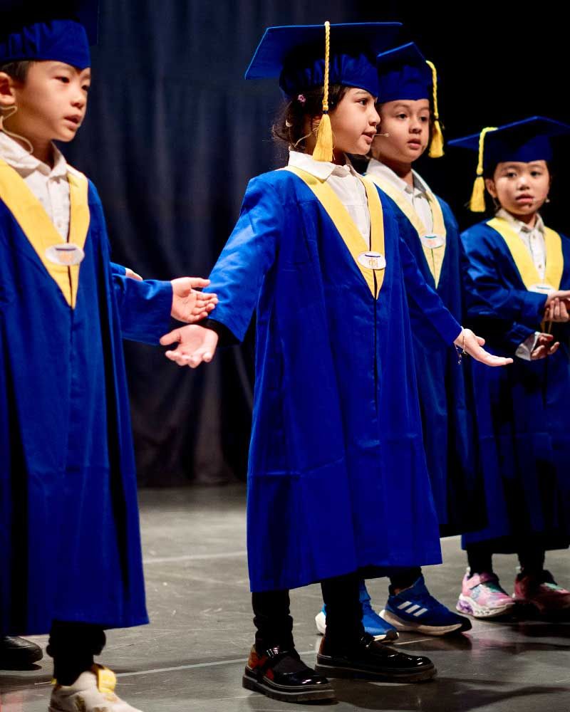 A group of young children wearing graduation gowns and caps are standing on a stage.