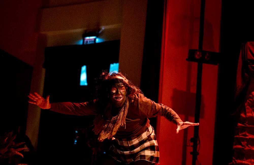 A woman is standing on a stage with her arms outstretched in a dark room.