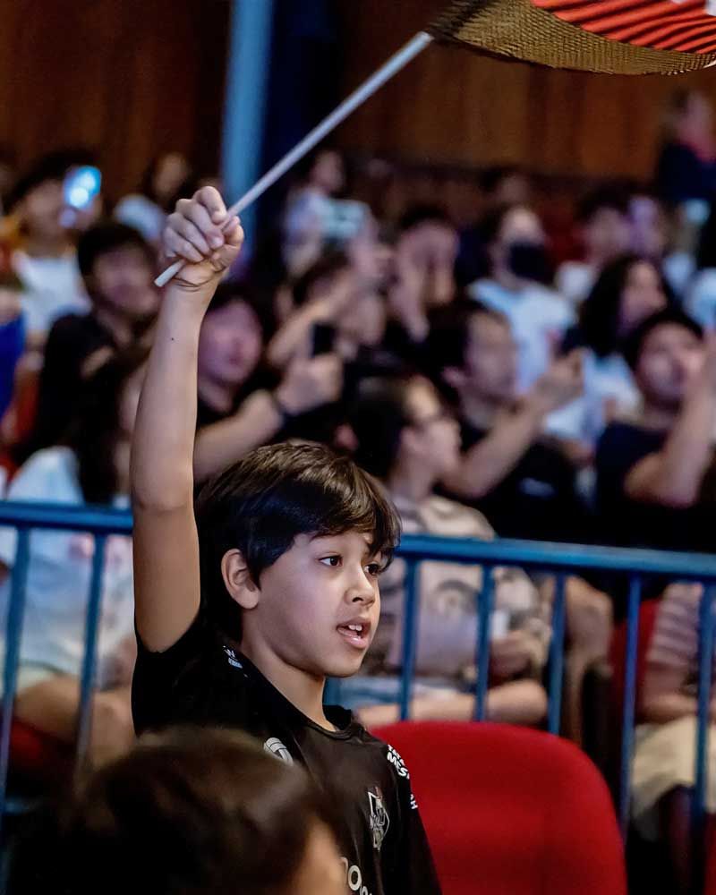 A young boy is holding up a flag in front of a crowd.