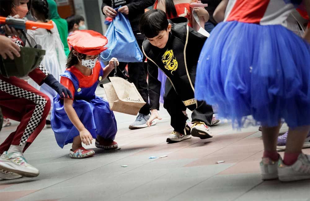 A group of children dressed in costumes are playing a game on the sidewalk.