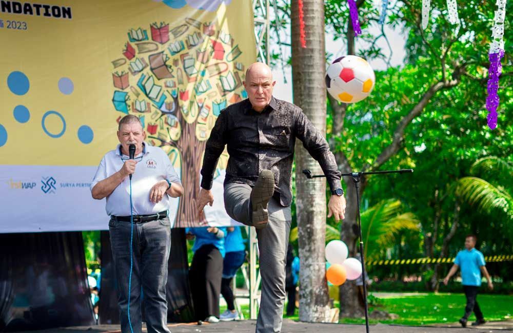 Two men are standing on a stage with a soccer ball in the background.