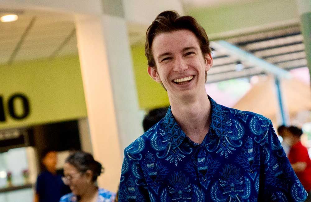 A man in a blue shirt is smiling in front of a sign that says 10