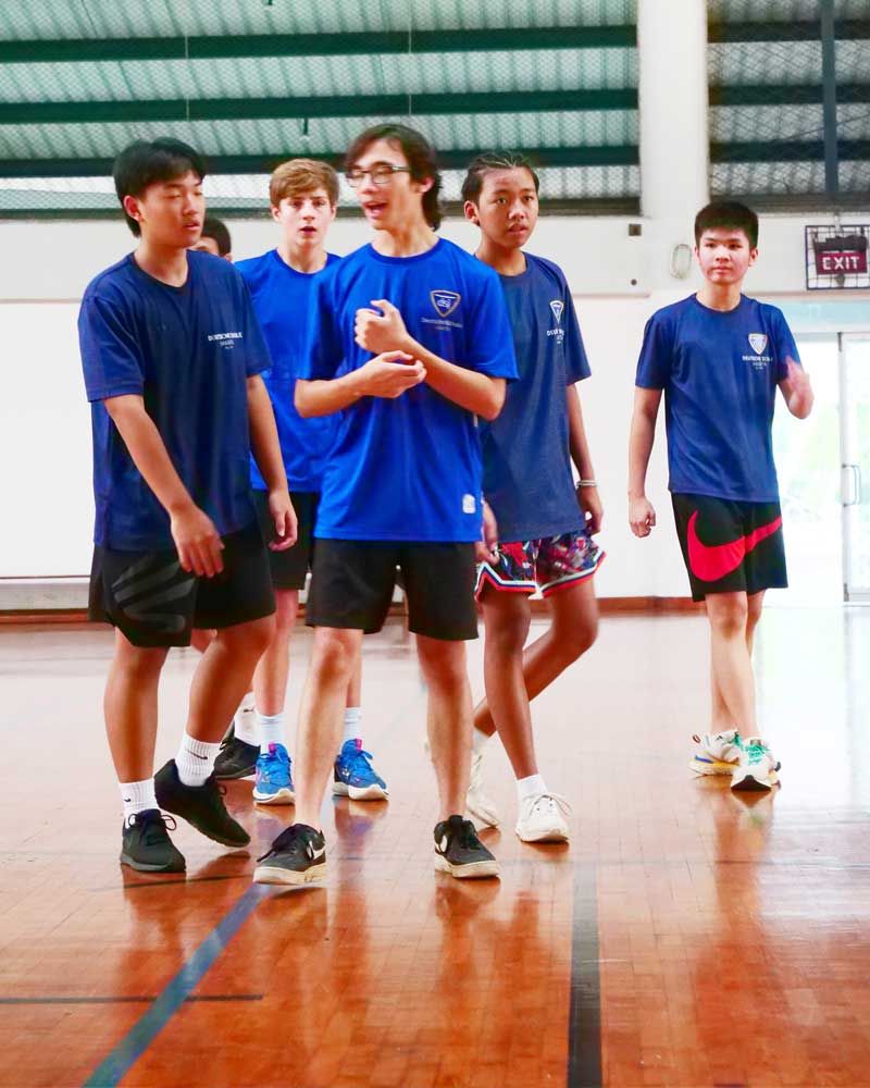 A group of young men in blue shirts are standing on a basketball court