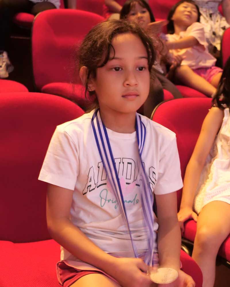 A young girl wearing a medal around her neck is sitting in a theater