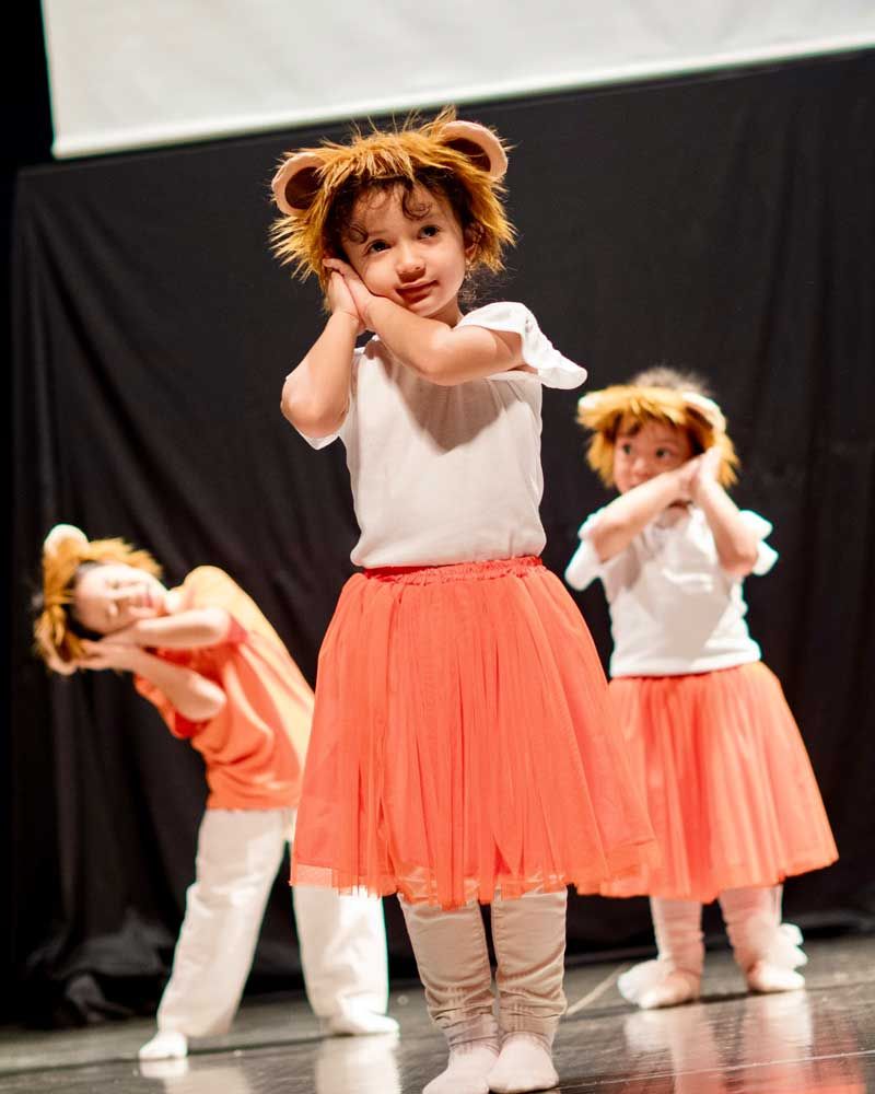 Three little girls are dancing on a stage and one of them is wearing a lion costume.