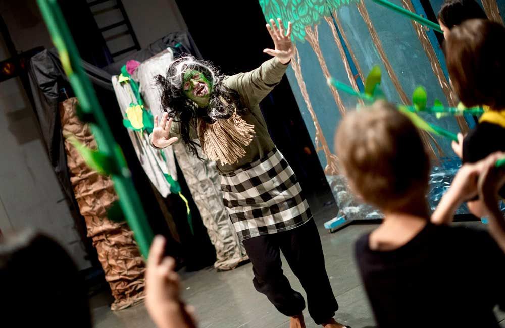 A woman in a witch costume is standing in front of a group of children.