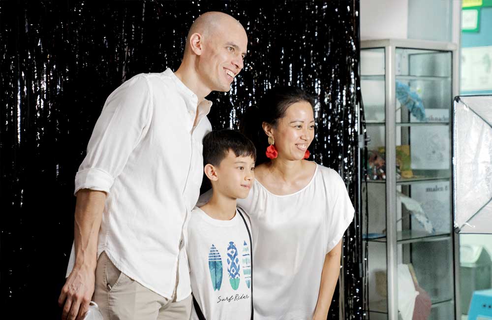 A man , woman and child are posing for a picture in front of a black curtain.