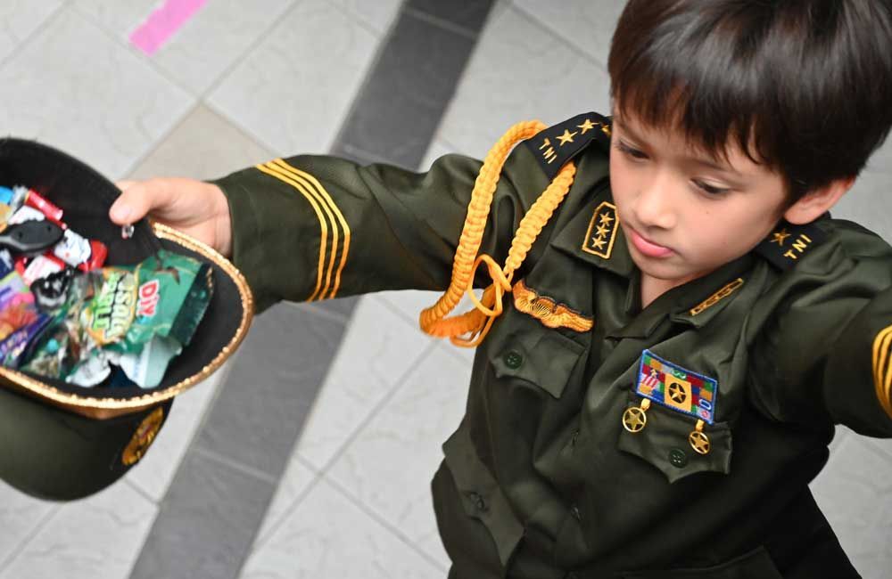 A young boy in a military uniform is holding a bowl of candy
