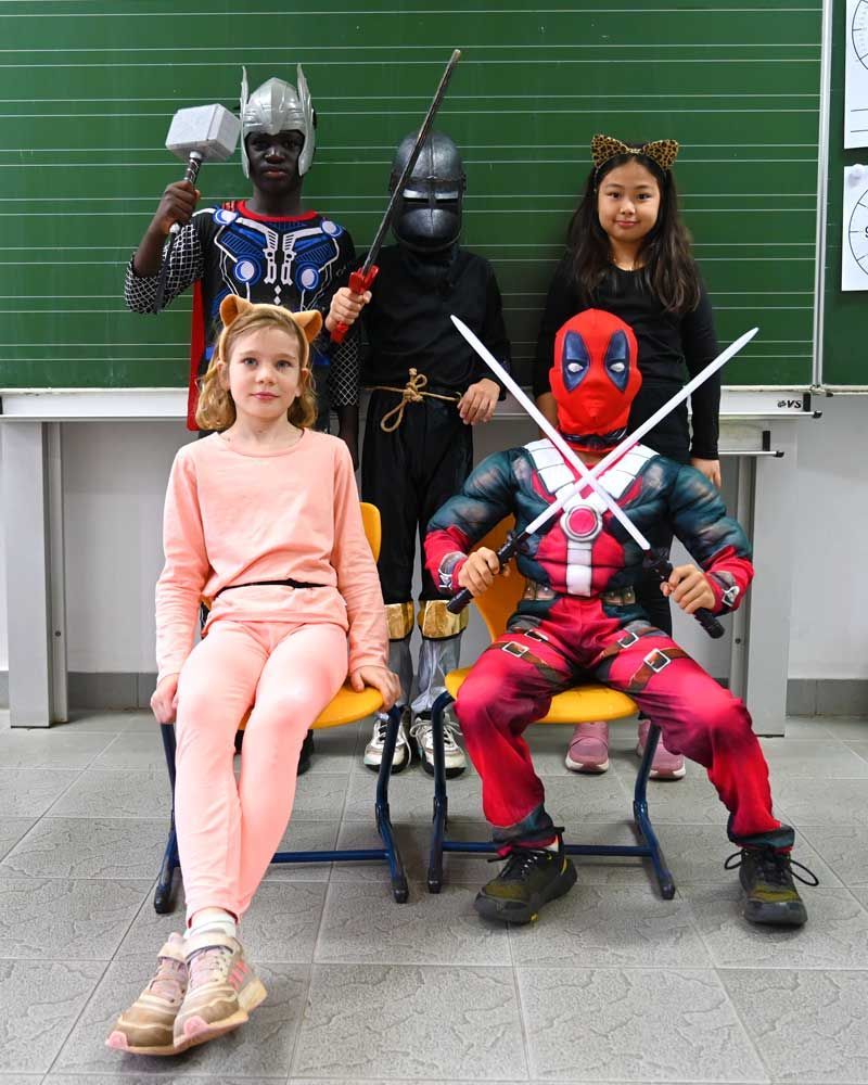 A group of children dressed in costumes are posing for a picture in front of a blackboard.