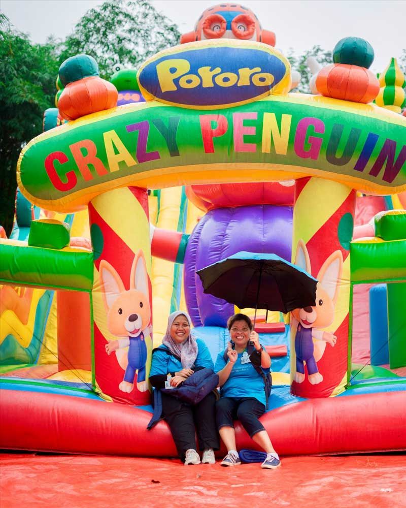 Two women are sitting in front of a colorful bouncy house.