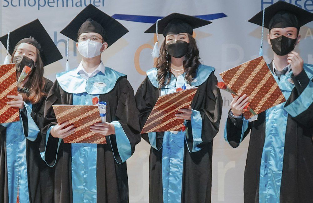 A group of graduates wearing masks and gowns are standing next to each other.