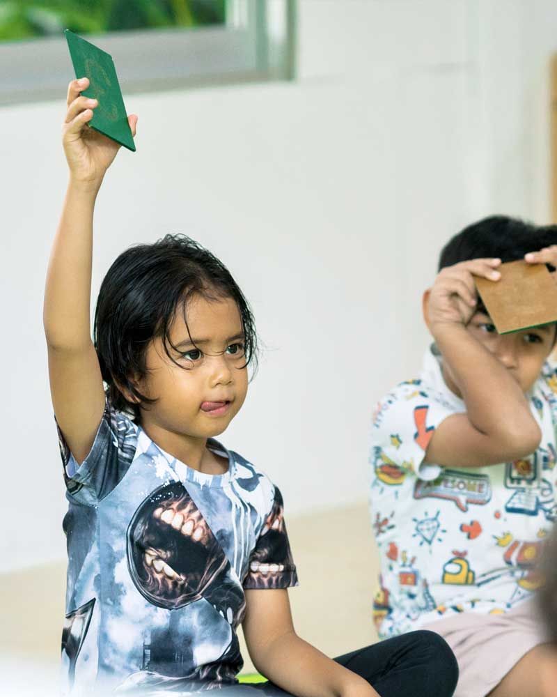 A little girl is raising her hand to answer a question.