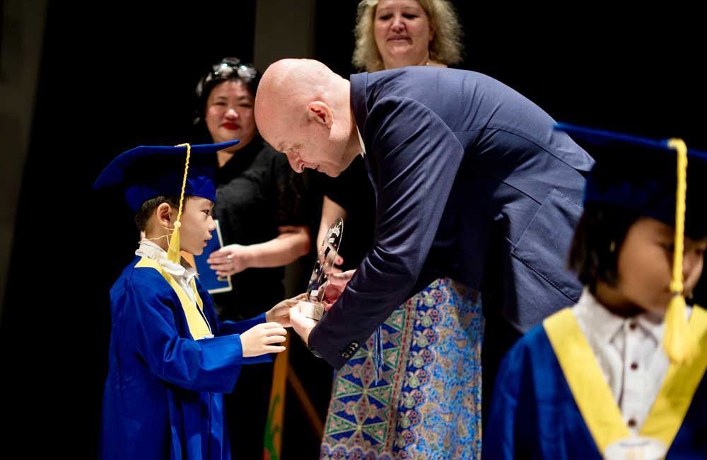 A man is kneeling down next to a girl in a graduation cap and gown.