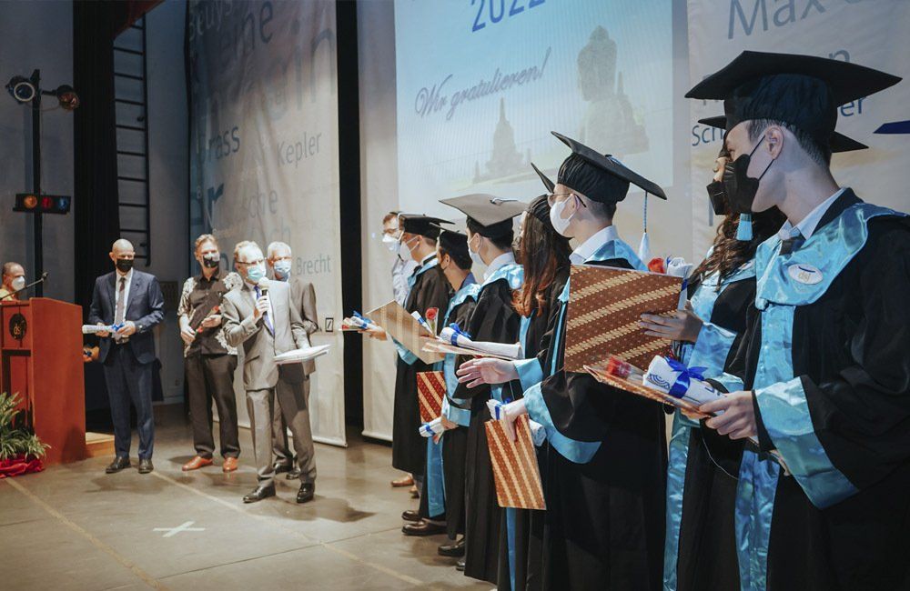 A group of graduates are standing on a stage holding their diplomas.