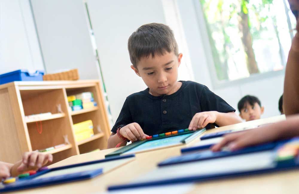 A young boy is sitting at a table in a classroom playing with a toy.