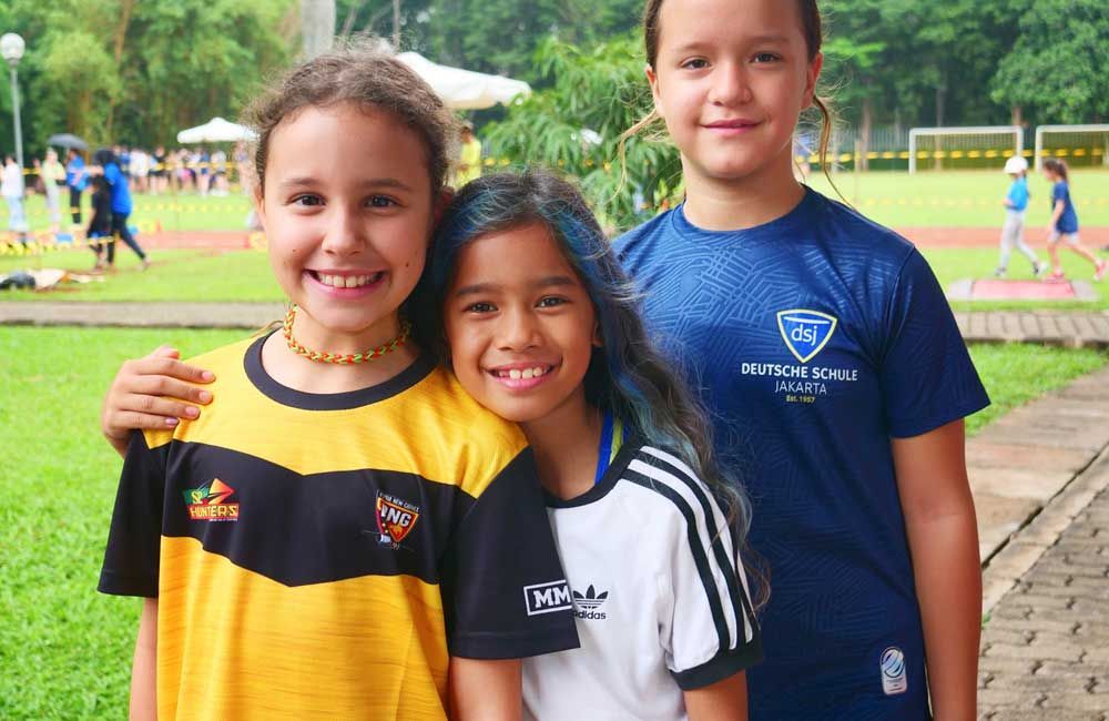 Three young girls are posing for a picture in front of a soccer field.