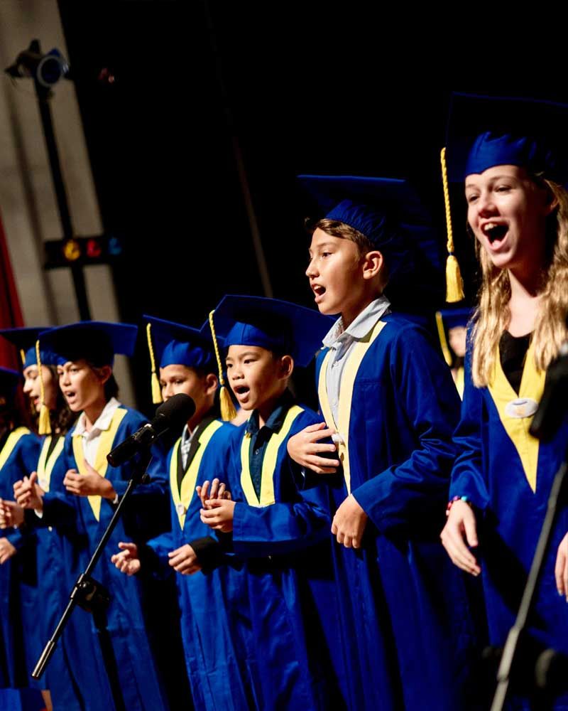 A group of children in graduation gowns and caps singing into microphones