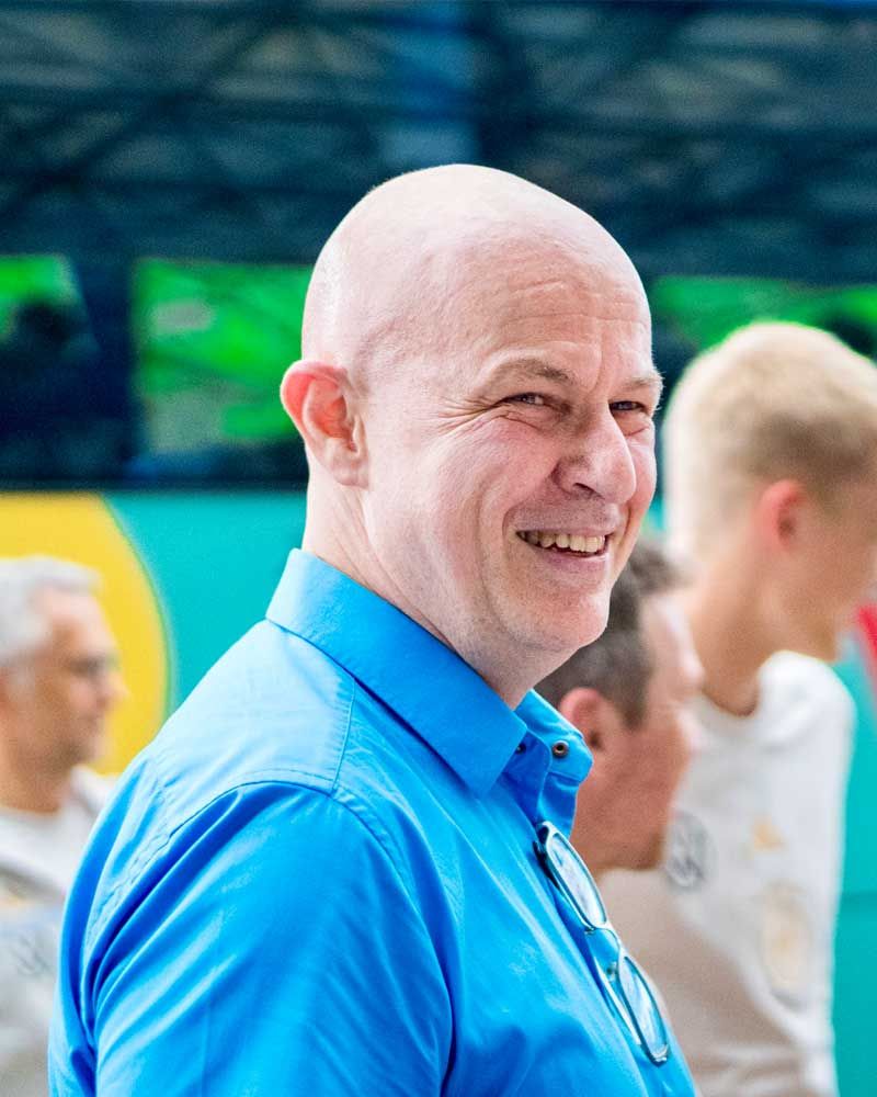 A bald man is wearing a blue shirt and smiling.