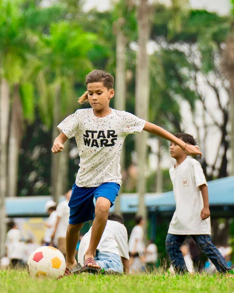 A young boy in a star wars shirt is kicking a soccer ball.