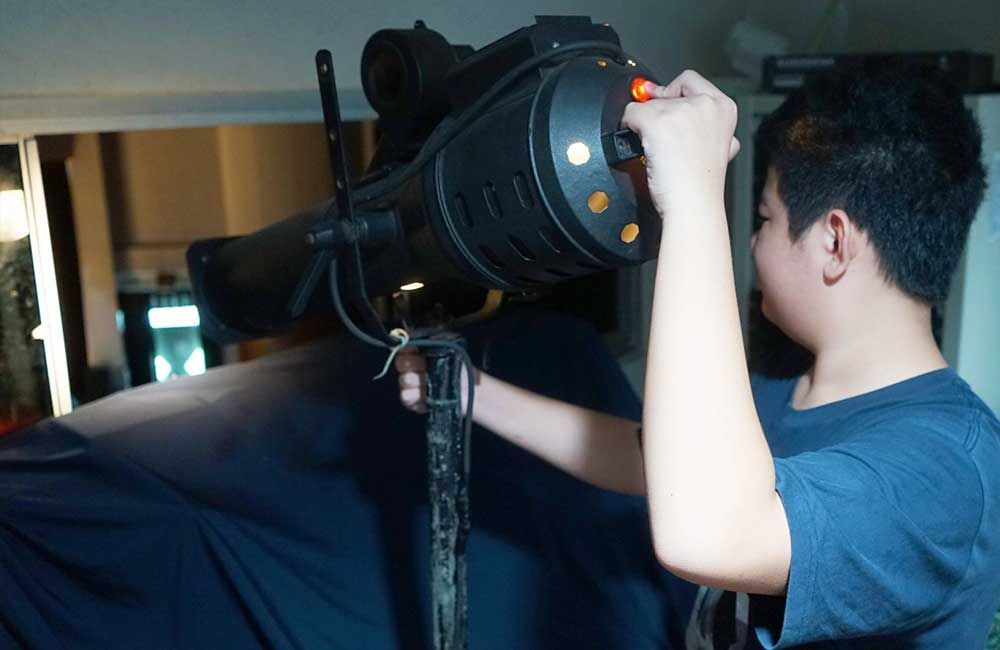 A young boy is adjusting a camera on a tripod.