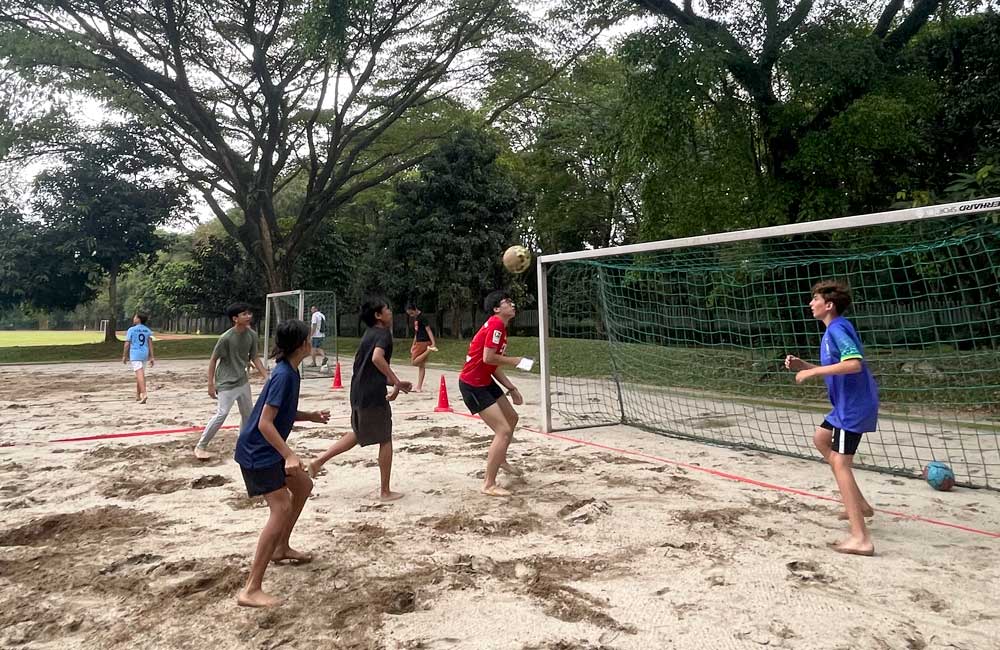 A group of children are playing soccer on a sandy field.