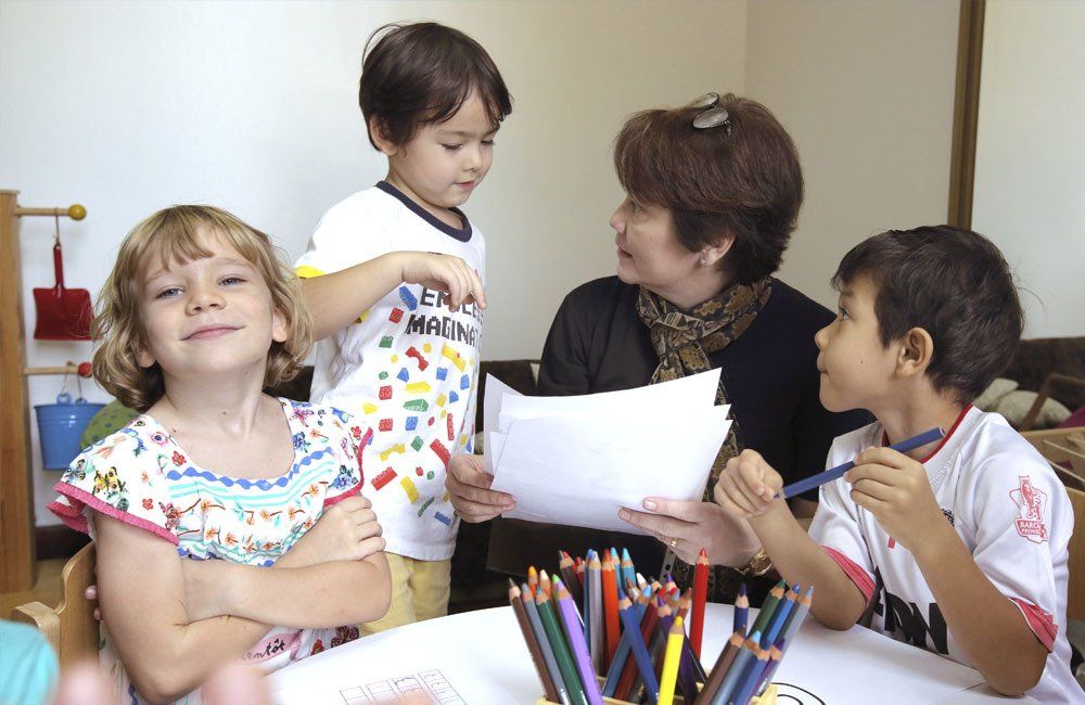 A woman is holding a piece of paper while two children sit at a table with colored pencils