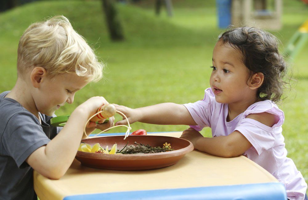 A boy and a girl are sitting at a table playing with a plate of food.