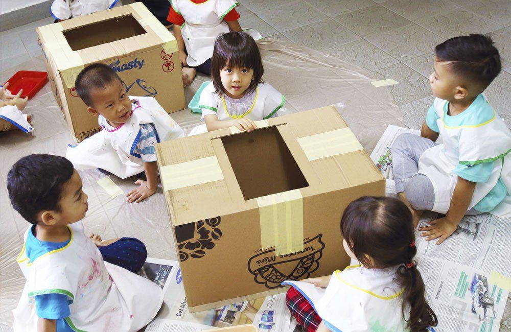 A group of children are sitting around a cardboard box that says priority