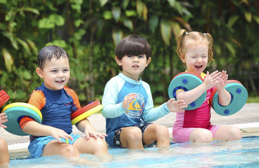 A group of children are sitting on the edge of a swimming pool.