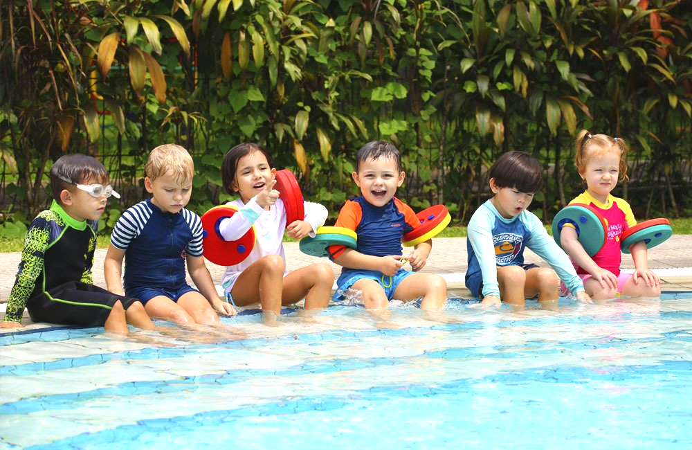 A group of children are sitting on the edge of a swimming pool.