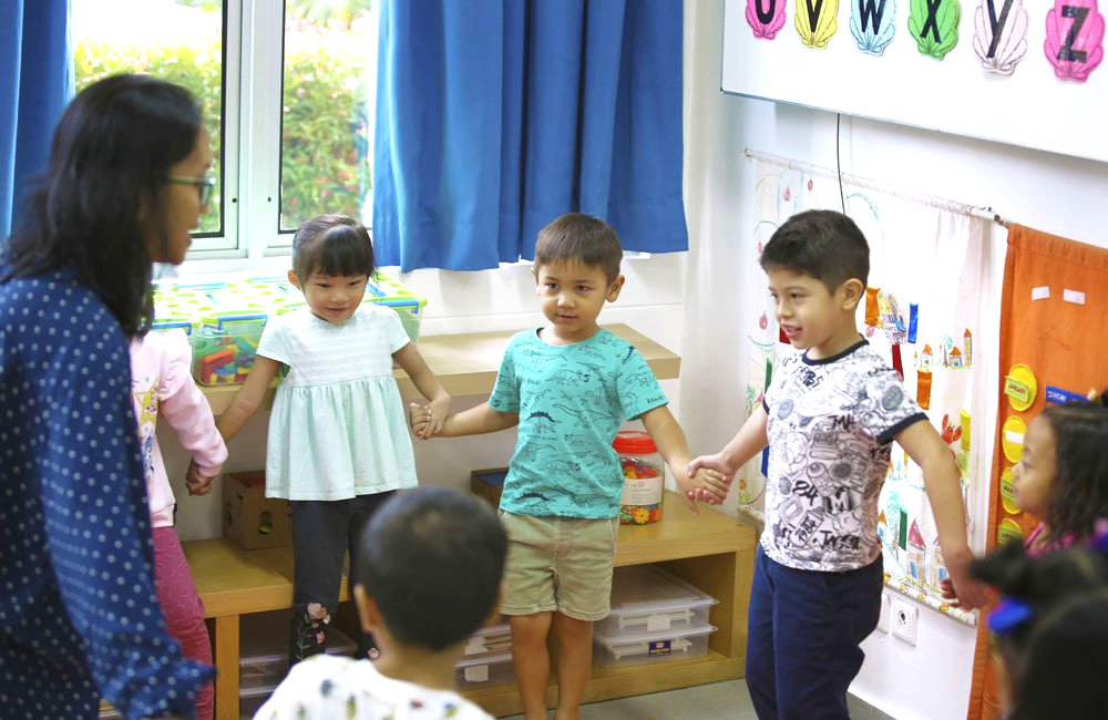A group of children are holding hands in a circle in a classroom.