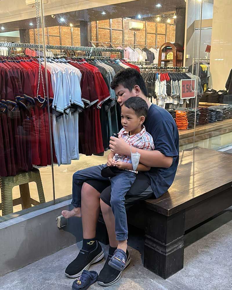 A man and a child are sitting on a bench in front of a clothing store.